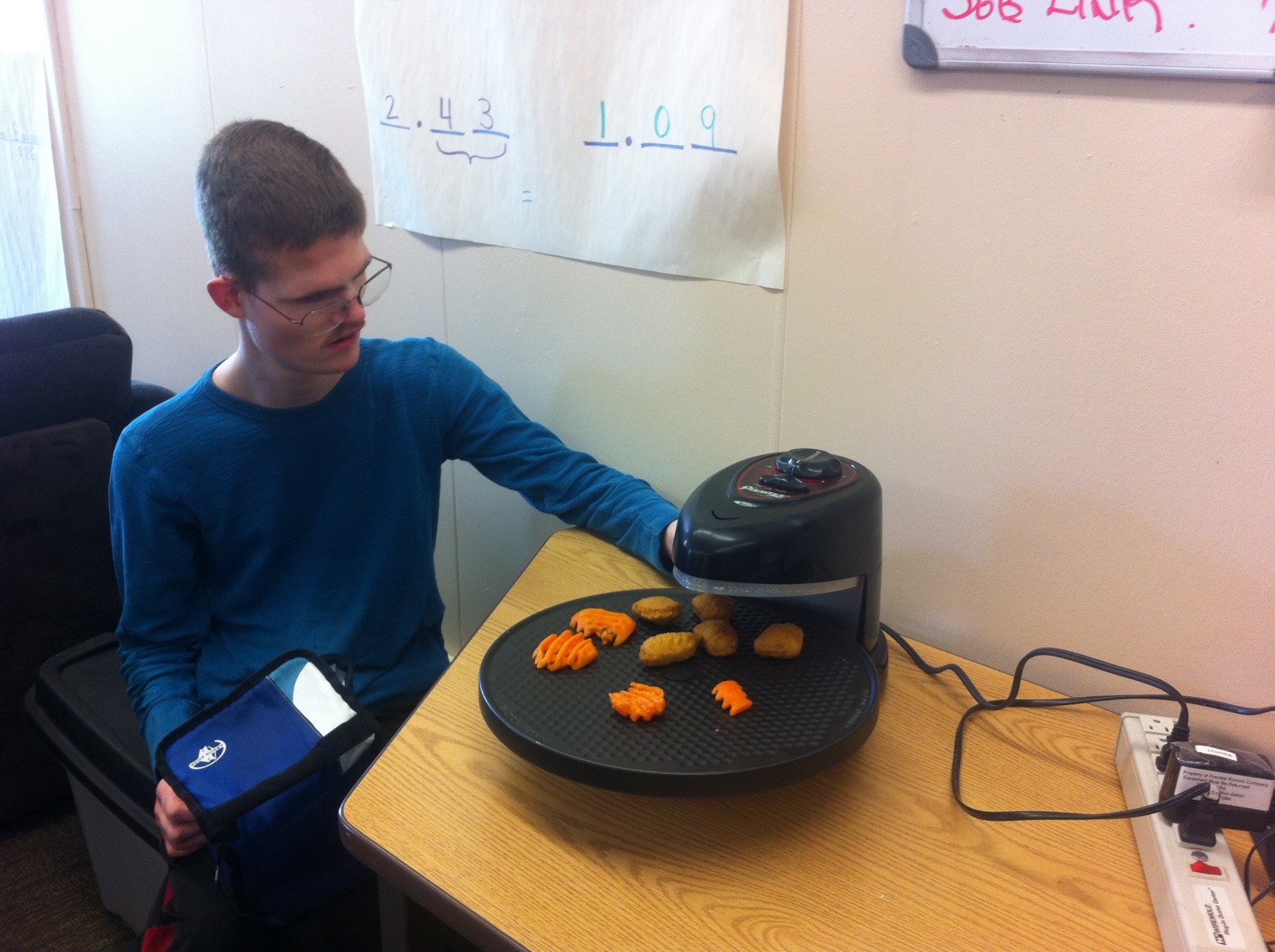 A young man who is deaf-blind is sitting at a table cooking carrots and potatoes on an electronic cooking device.