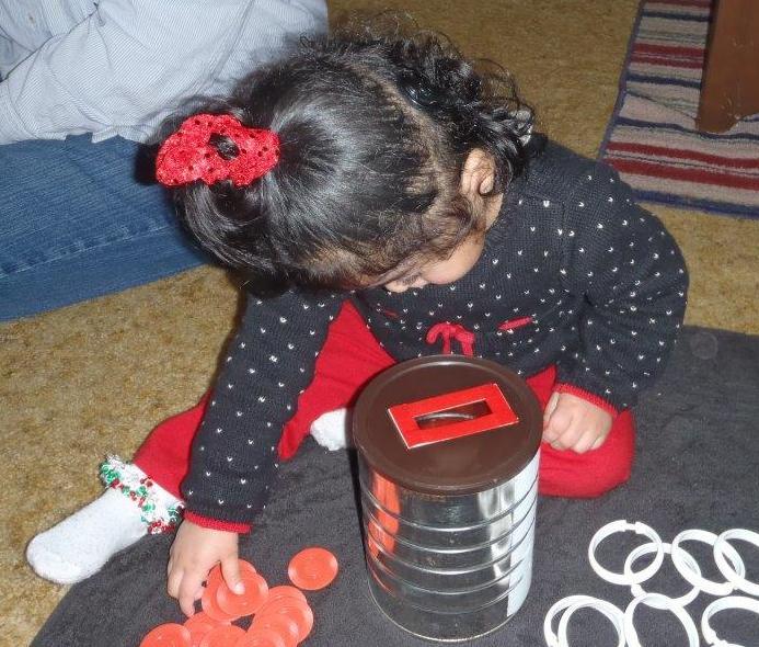 A child plays by putting discs and rings into a can.