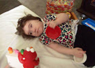 A child lays on a bed next to an Elmo toy.