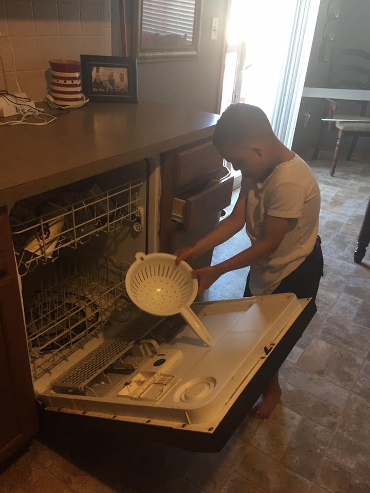 A young man who is deaf-blind is taking a dish out of a dishwasher.