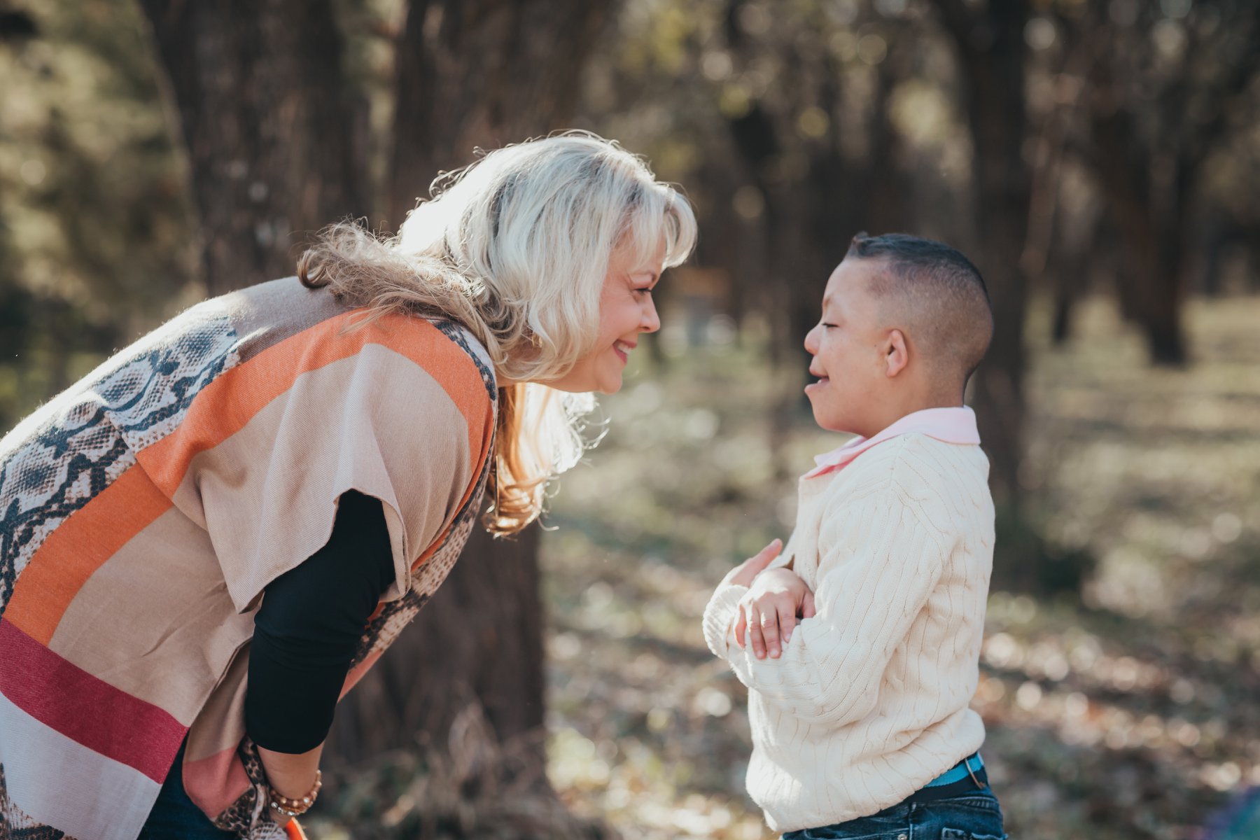 A 16-year-old boy who is deaf-blind and his mom, outside in a place with trees in the background. The mother is leaning toward the boy. Both are smiling broadly.