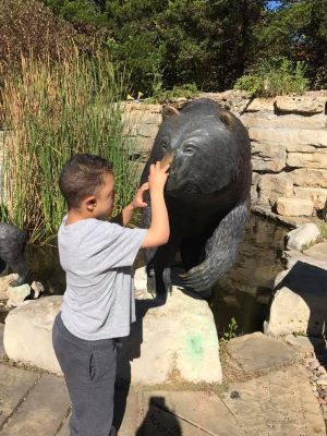 A boy at a zoo is feeling a statue of a bear with both hands.