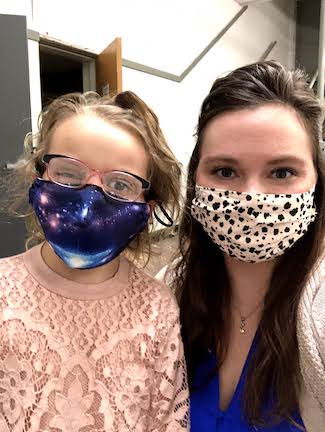An adult woman who is a teacher, and a girl who is a student with deaf-blindness, standing side by side looking at the camera. Both are wearing masks over their mouths because of the COVID-19 pandemic.