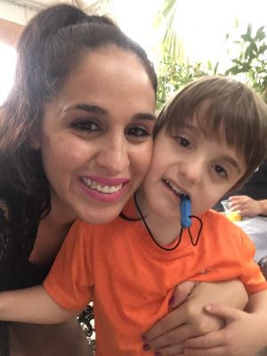 A mother with her arms around her young son who is deaf-blind. Both smiling for the camera.