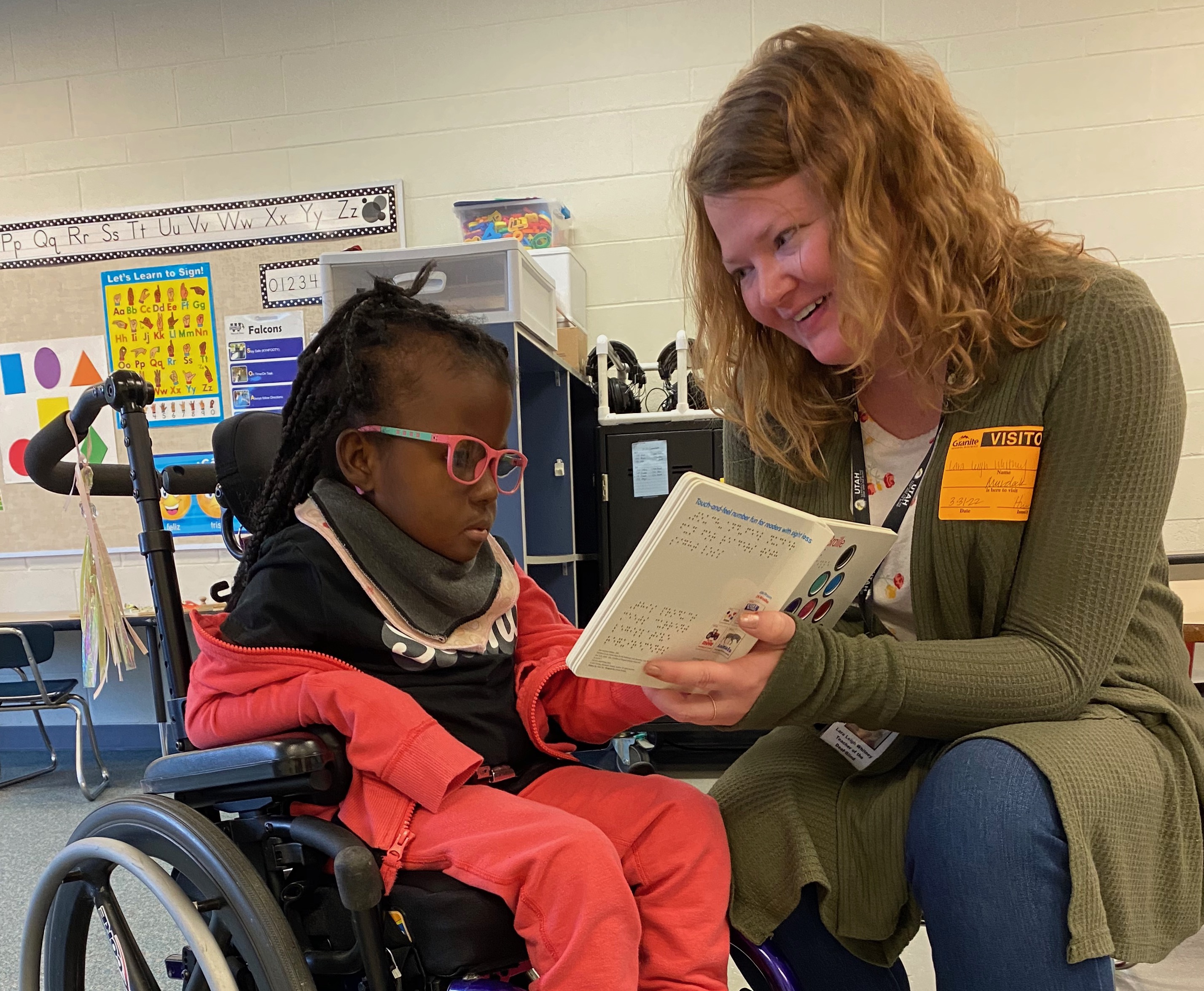 Lara reads a book with her student in a wheelchair.