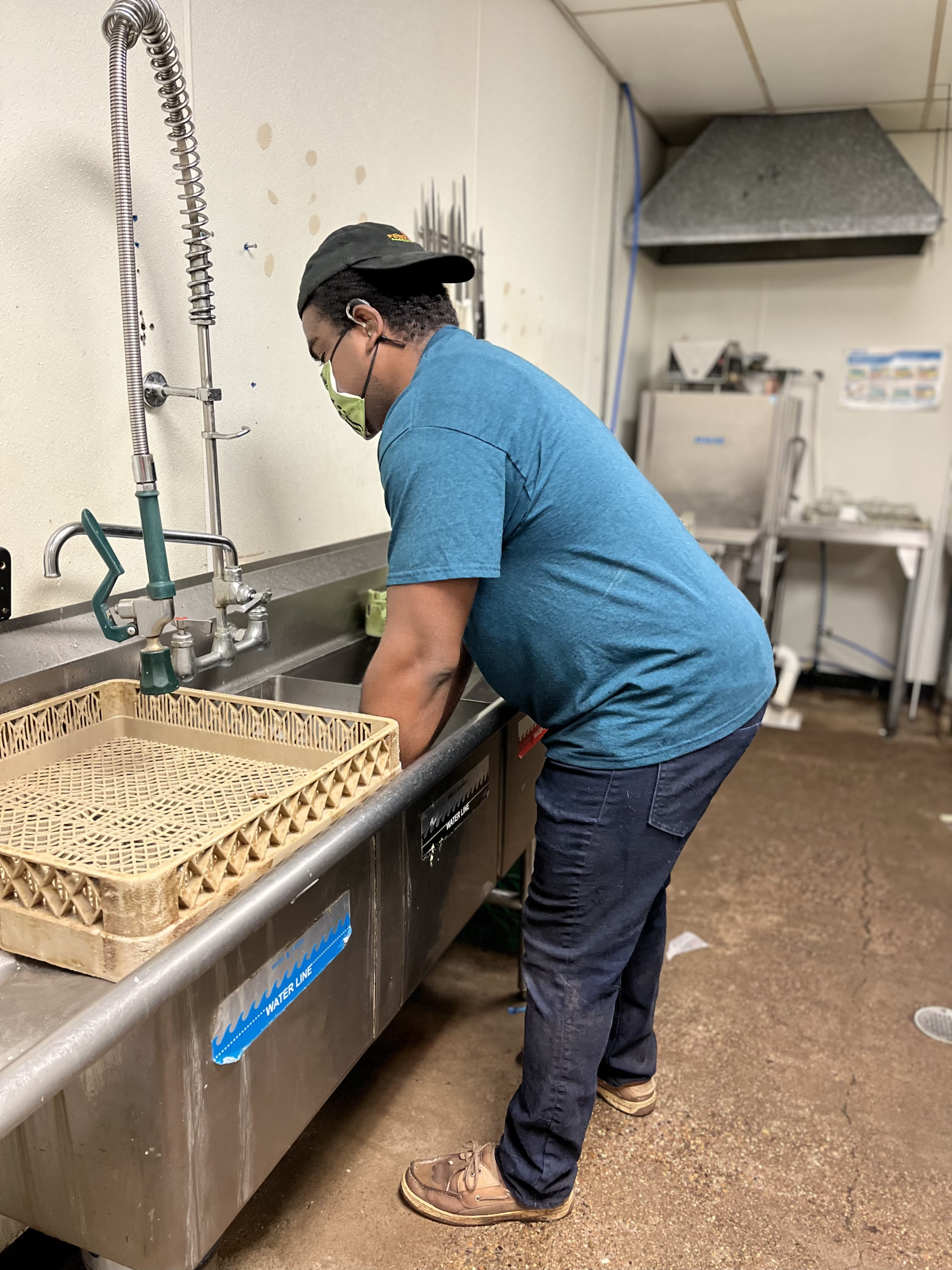 A man stands at a commercial sink and washes dishes.