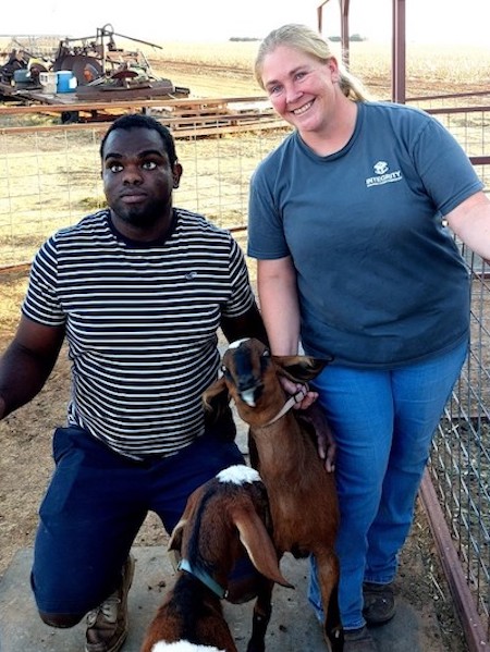 A man and woman stand next to two goats at a farm.