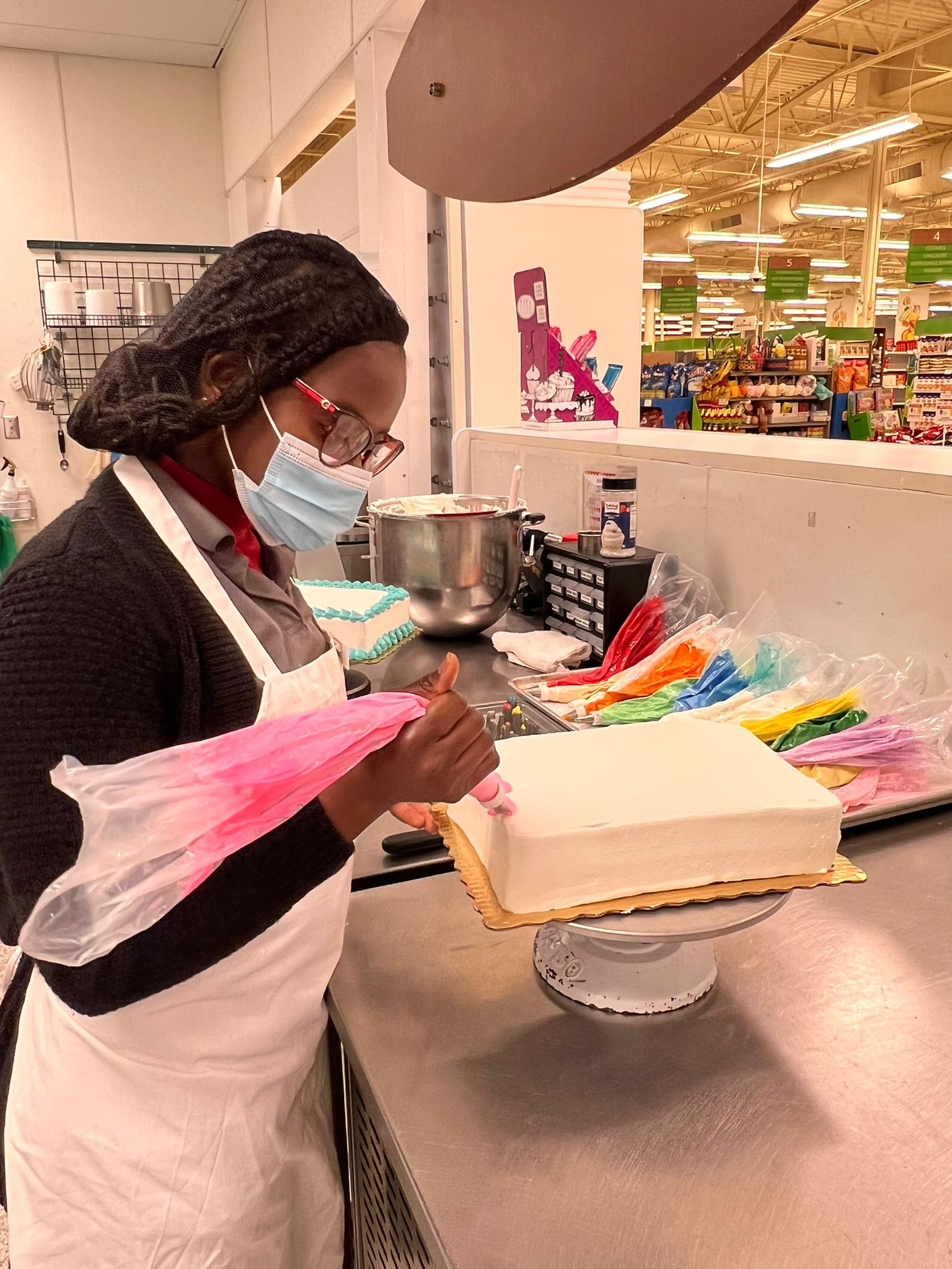 A woman decorates a white cake with different colored icing bags.