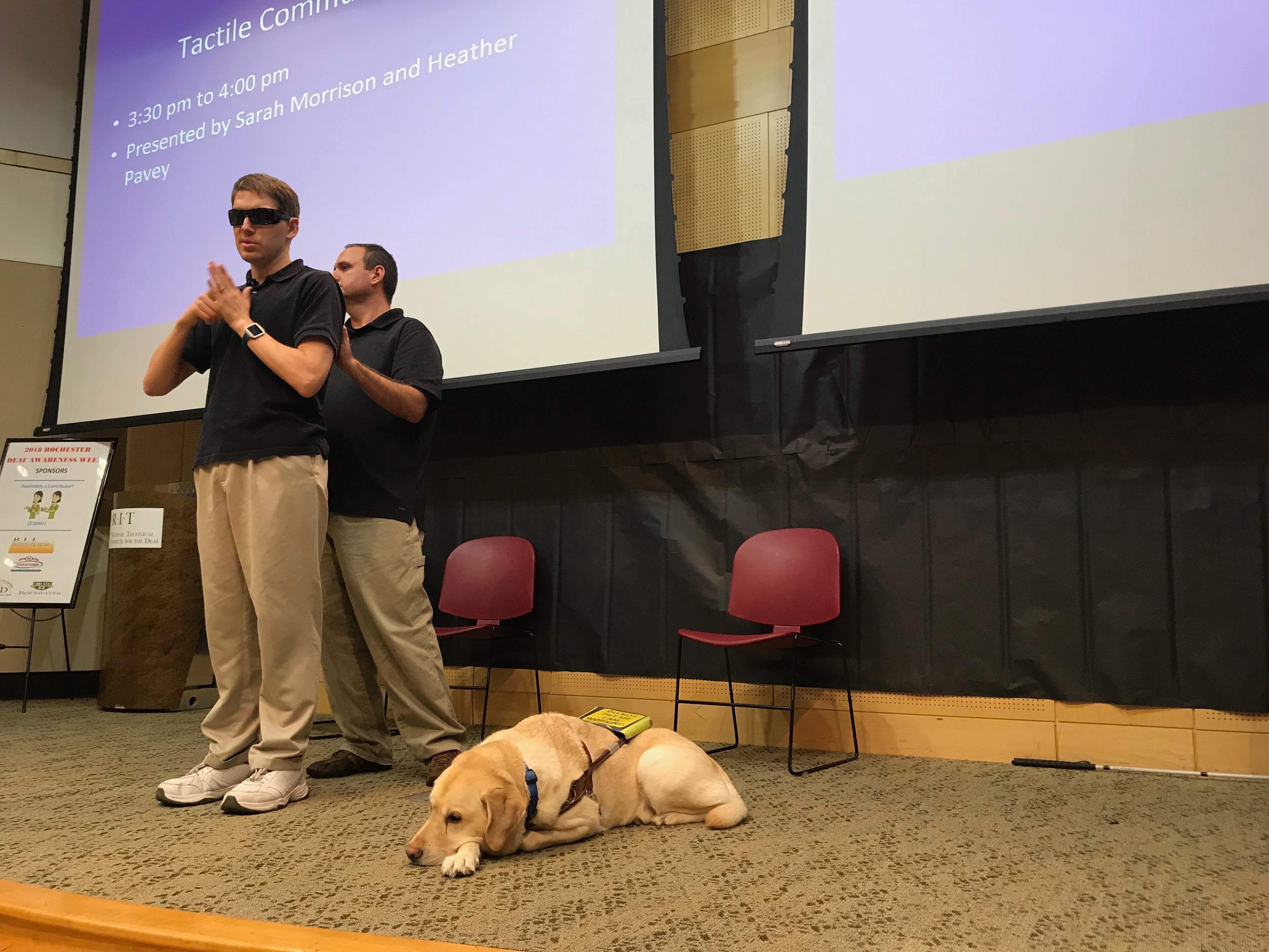 Jason presenting with a interpreting providing environmental information a guide dog next to Jason.