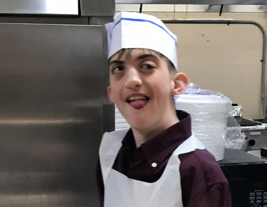 Young adult man in restaurant kitchen wearing cooks hat and apron.