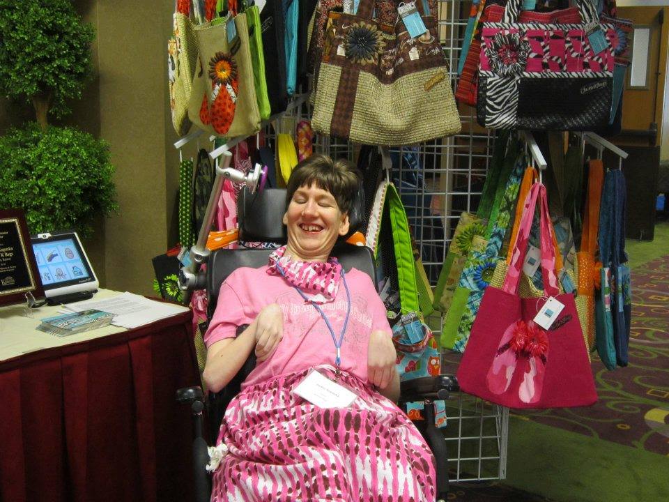 A woman in wearing pink with short dark hair is sitting in front of several bags hanging