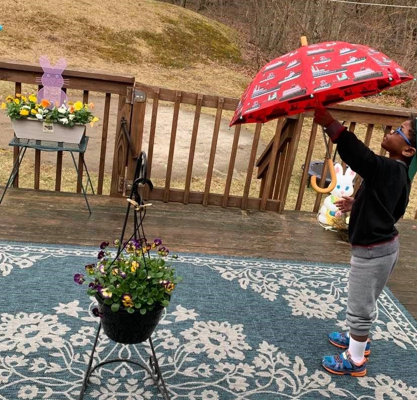 6-year-old boy standing on a deck holding a red umbrella with pictures of boats on it.