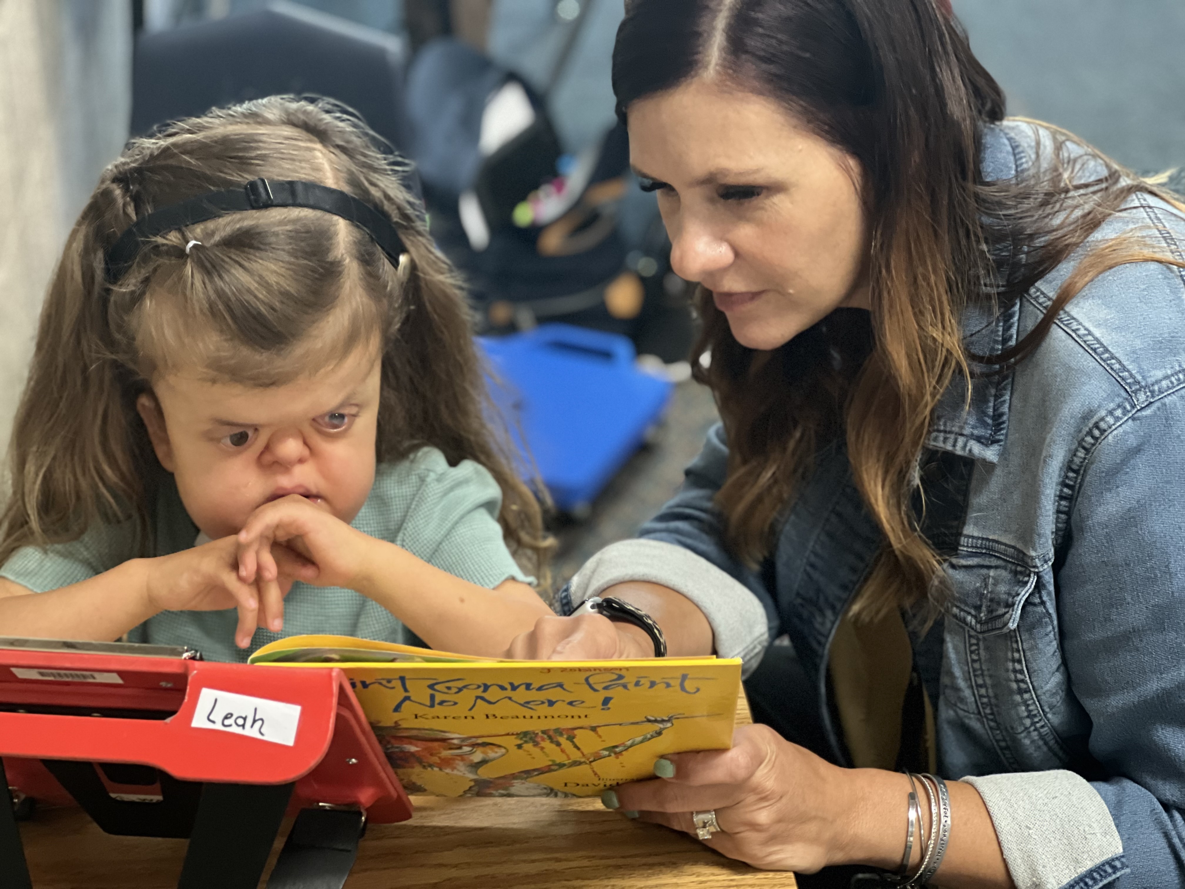 A teacher and young girl who is deaf-blind read a book together.