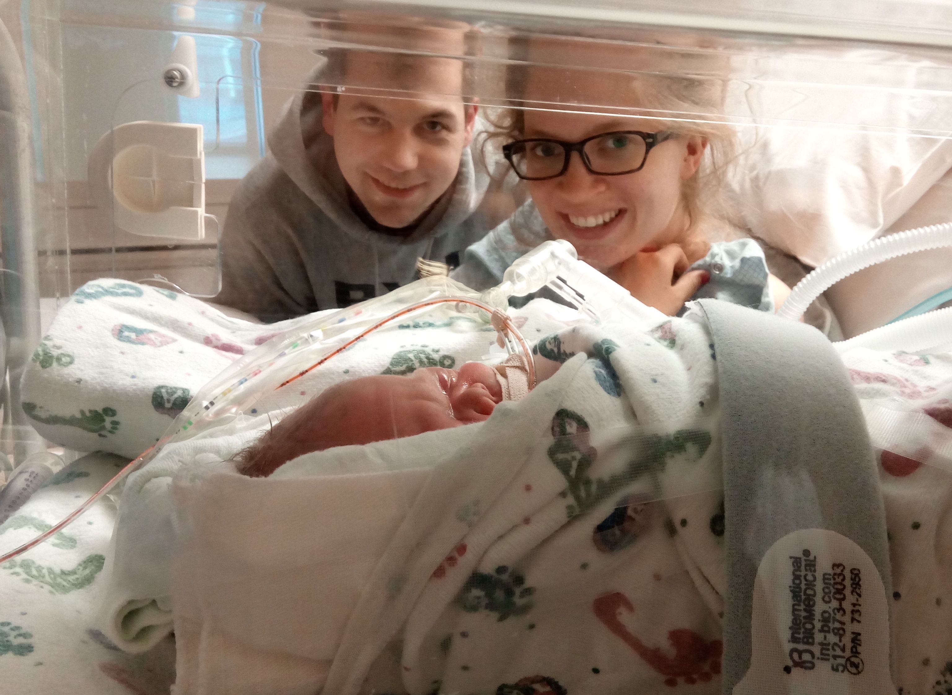 Baby Kimball in the NICU. Mom an dad are standing behind.