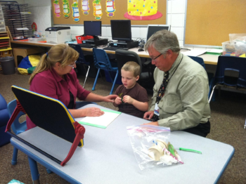 Boy with deaf-blindness sitting at a table with two educators.