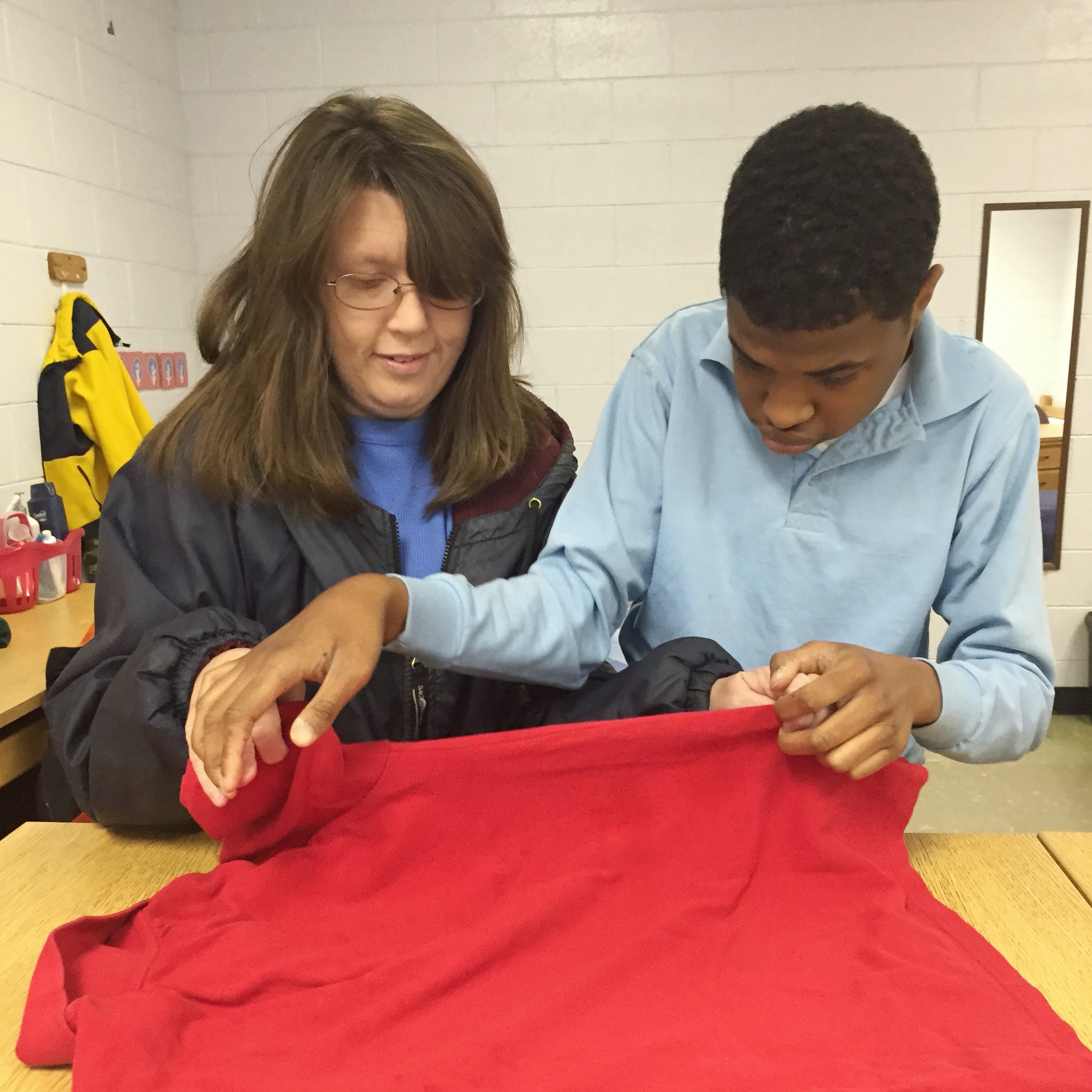 A women helping a young man fold shirt.