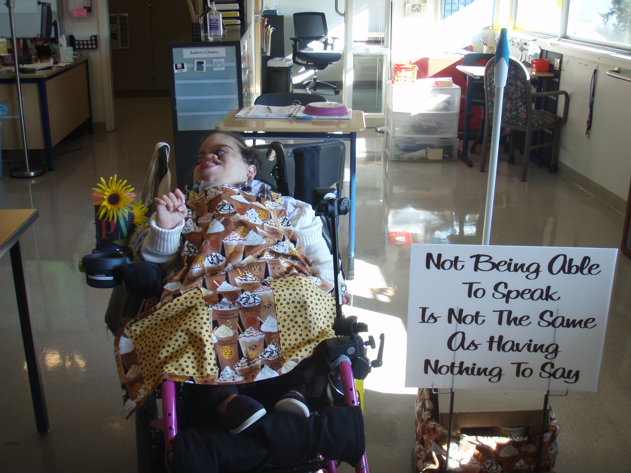 Miranda in her wheeler chair with poster that says, "Not being able to speak is not the same as having nothing to say".