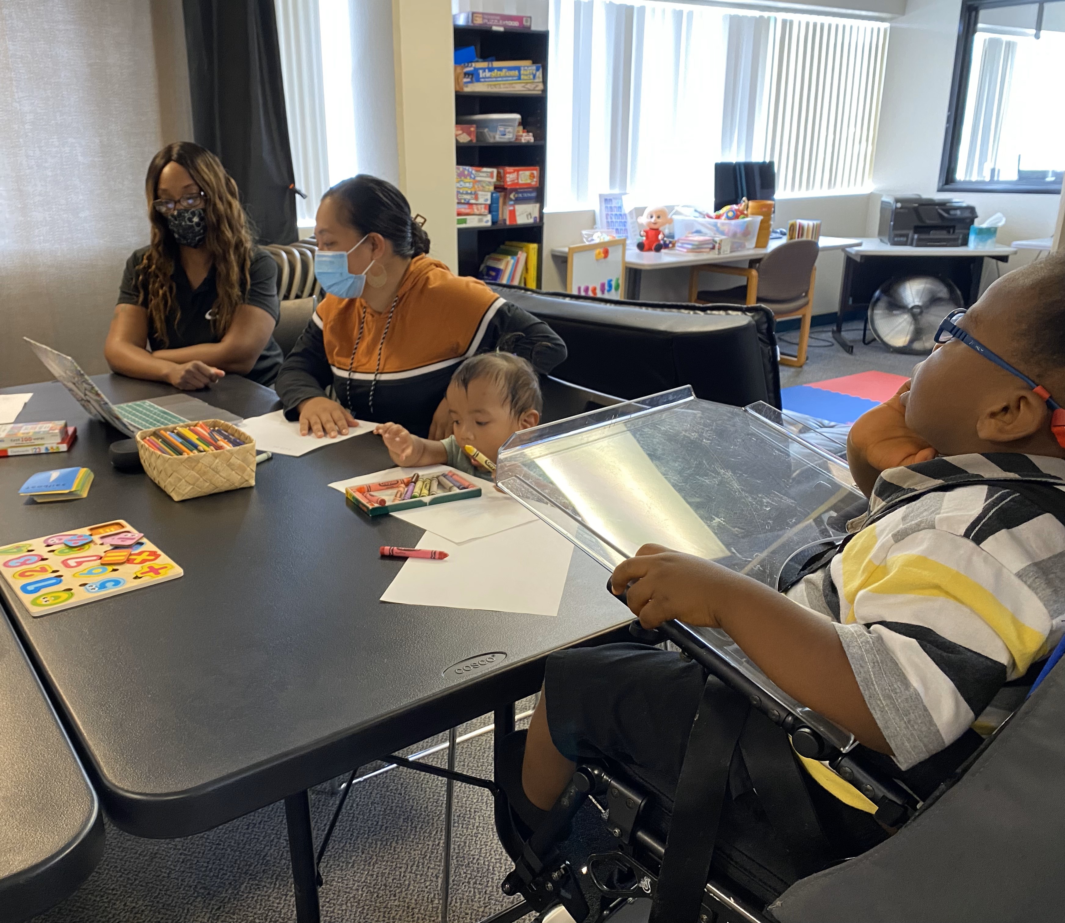 A family engagement coordinator goes over resources with a mom while a daughter is coloring. A boy looks on.