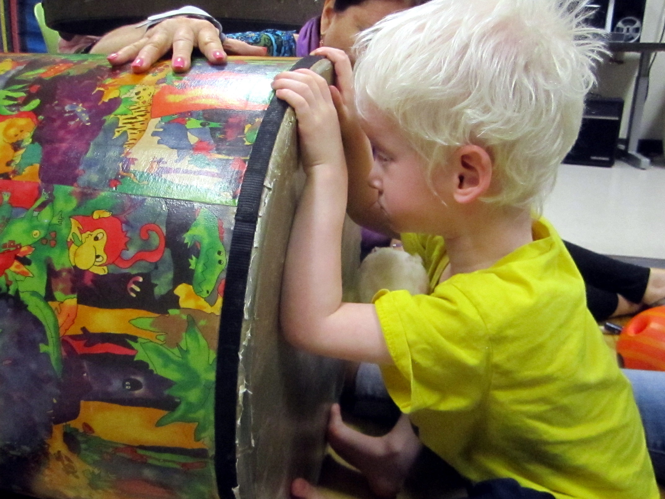 A young boy leans and touches drum.