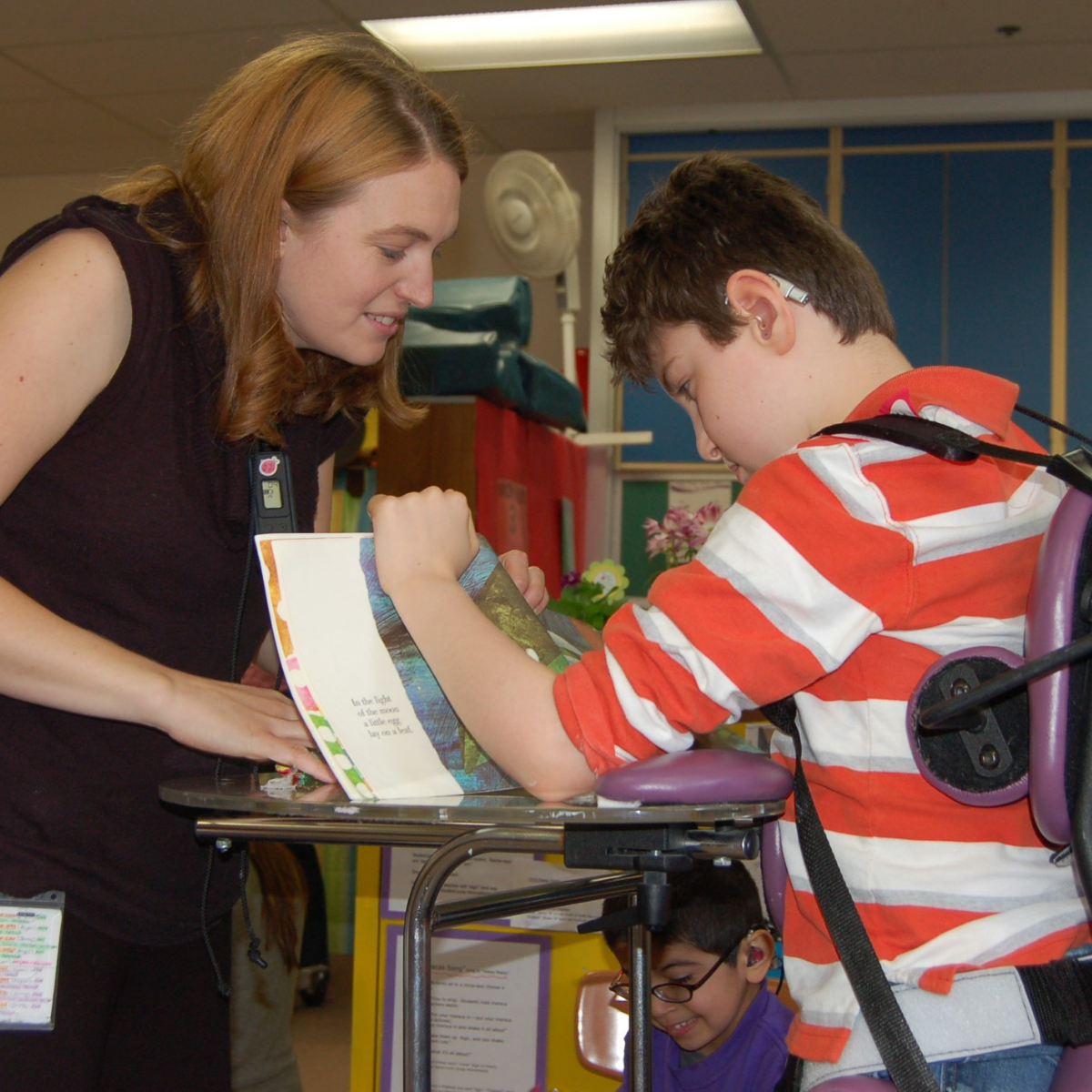 A teacher interacts with her student in a standing chair.