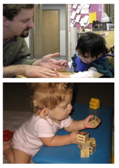 A teacher and young child with deaf-blindness sit at a table. The child's hands are touching the top of the teachers hands. Separately, a toddler is playing with blocks.