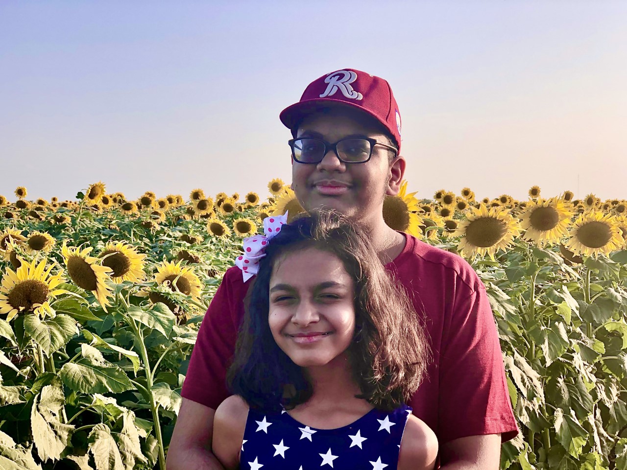 Two siblings standing in front of a sunflower field.