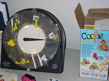 An adapted version of the game cootie: an arrow spins to taped down pieces of the game.