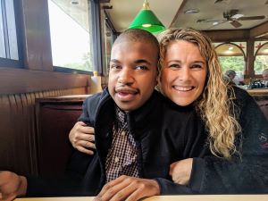 Young adult man who is deaf-blind in restaurant with a woman, posing for camera.
