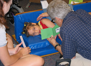 A man holds a book up close to a child's face, while she is laying down.