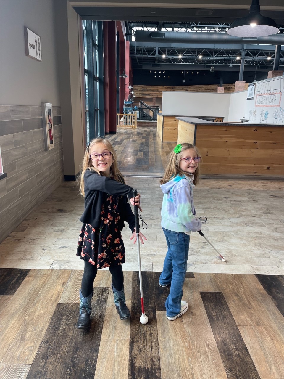 Two sisters walk in a building with their canes.