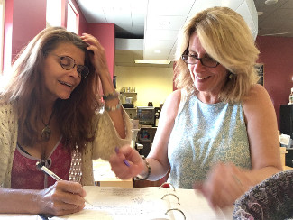 One woman coaches another through paperwork, while sitting at a table.