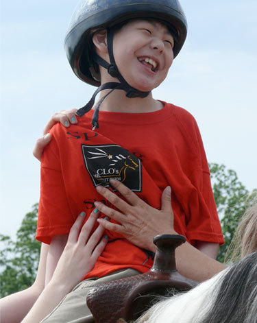 A young boy is sitting on top of. a horse while being supported by others.